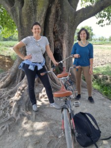 Two women under a large tree with bicycle